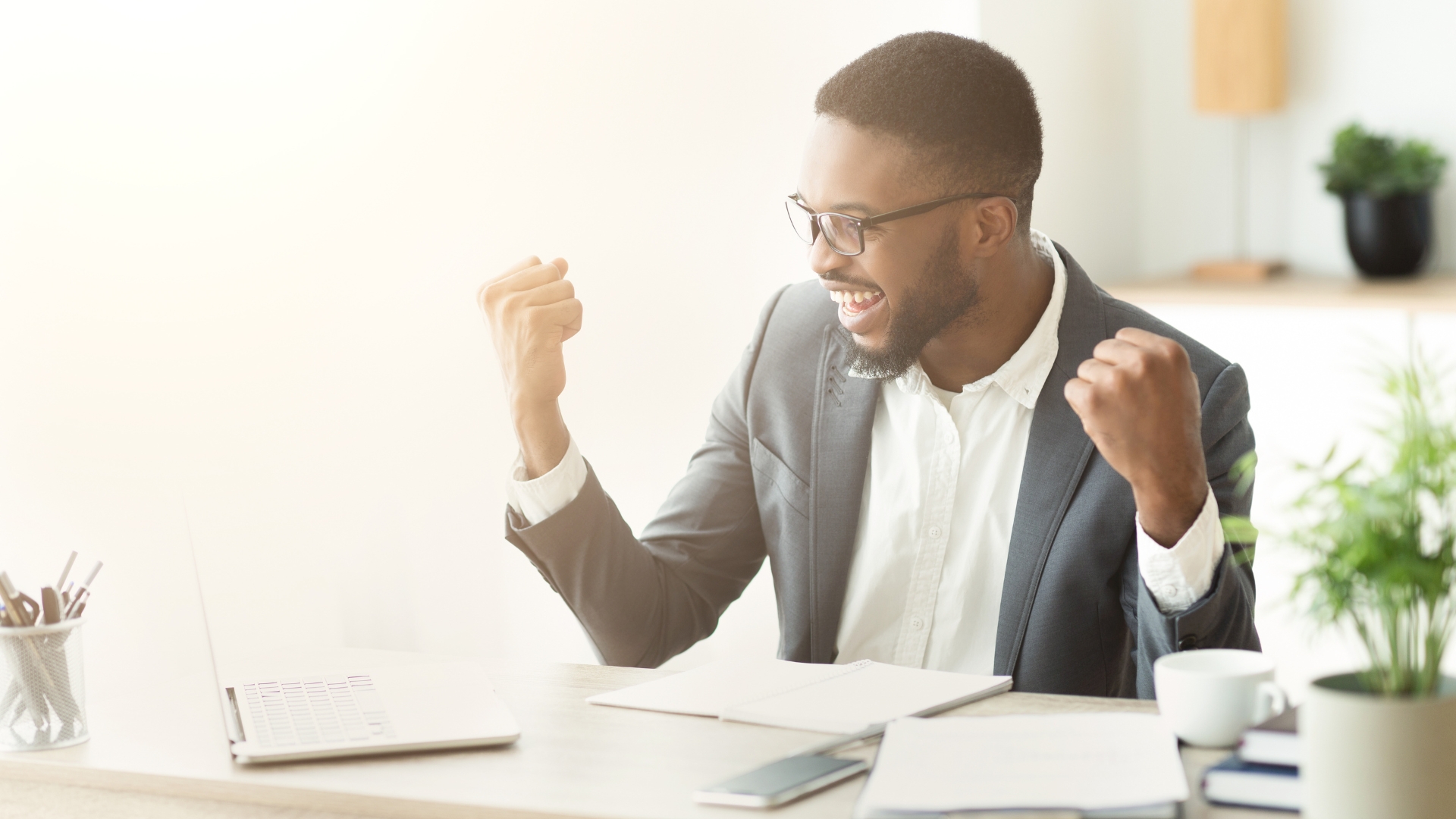 Black man in a suit celebrating a big win at work