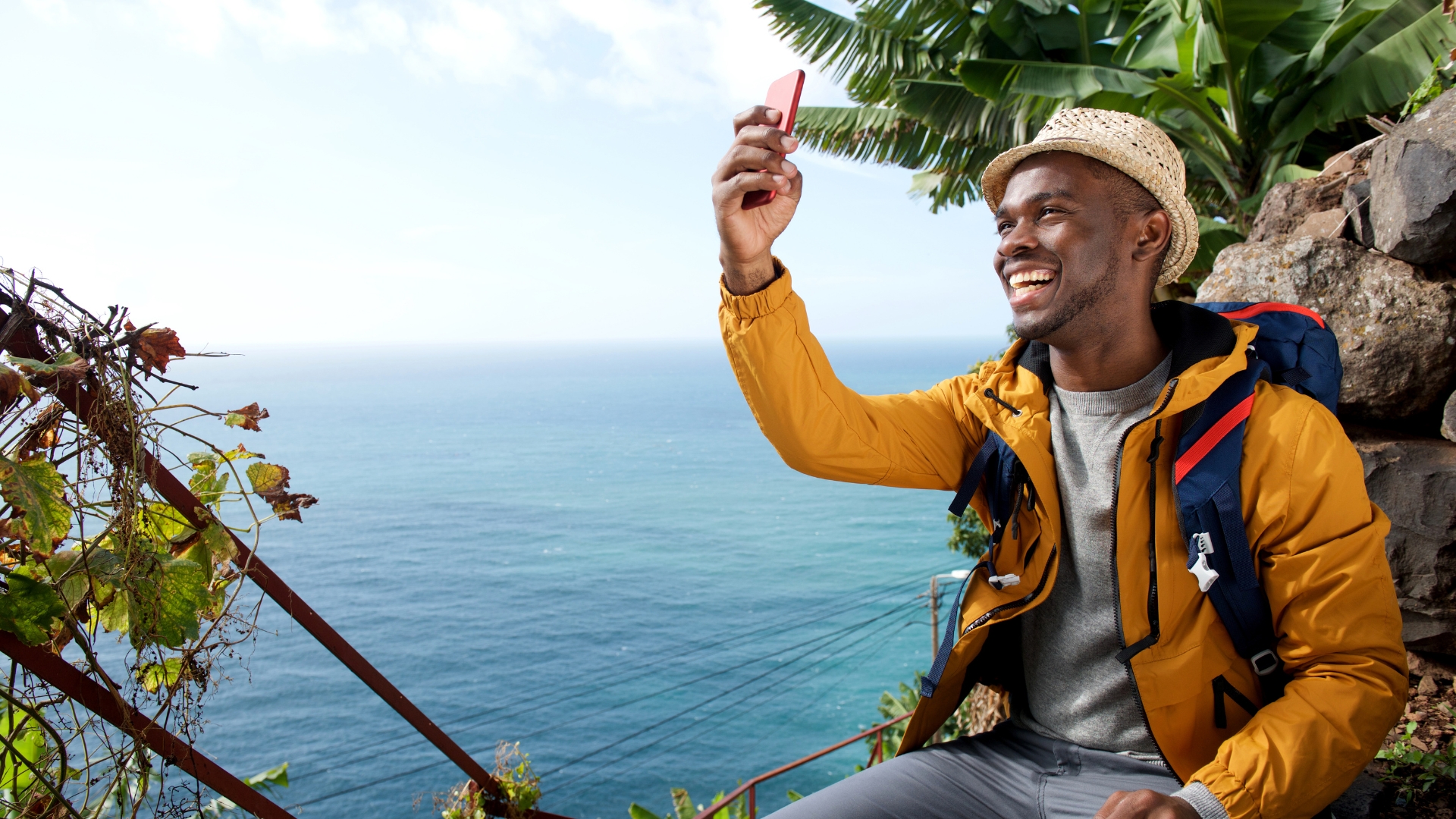 Black male traveler smiling on an island while taking a selfie - in promotion of Travel Noire City Guides