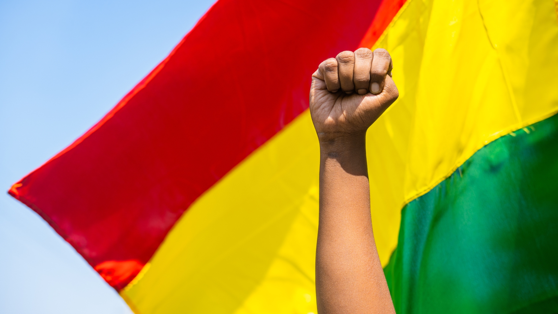 The fist of an African American male set in front of a red, yellow, and green flag