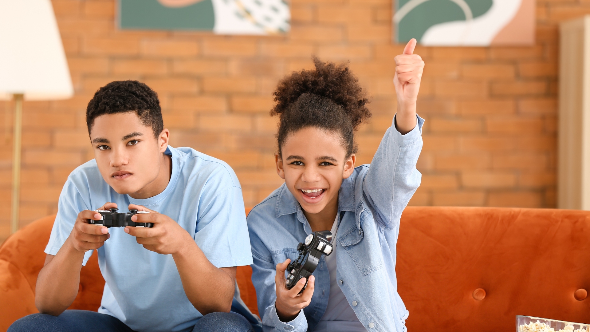2 Black teens sitting on the couch playing video games
