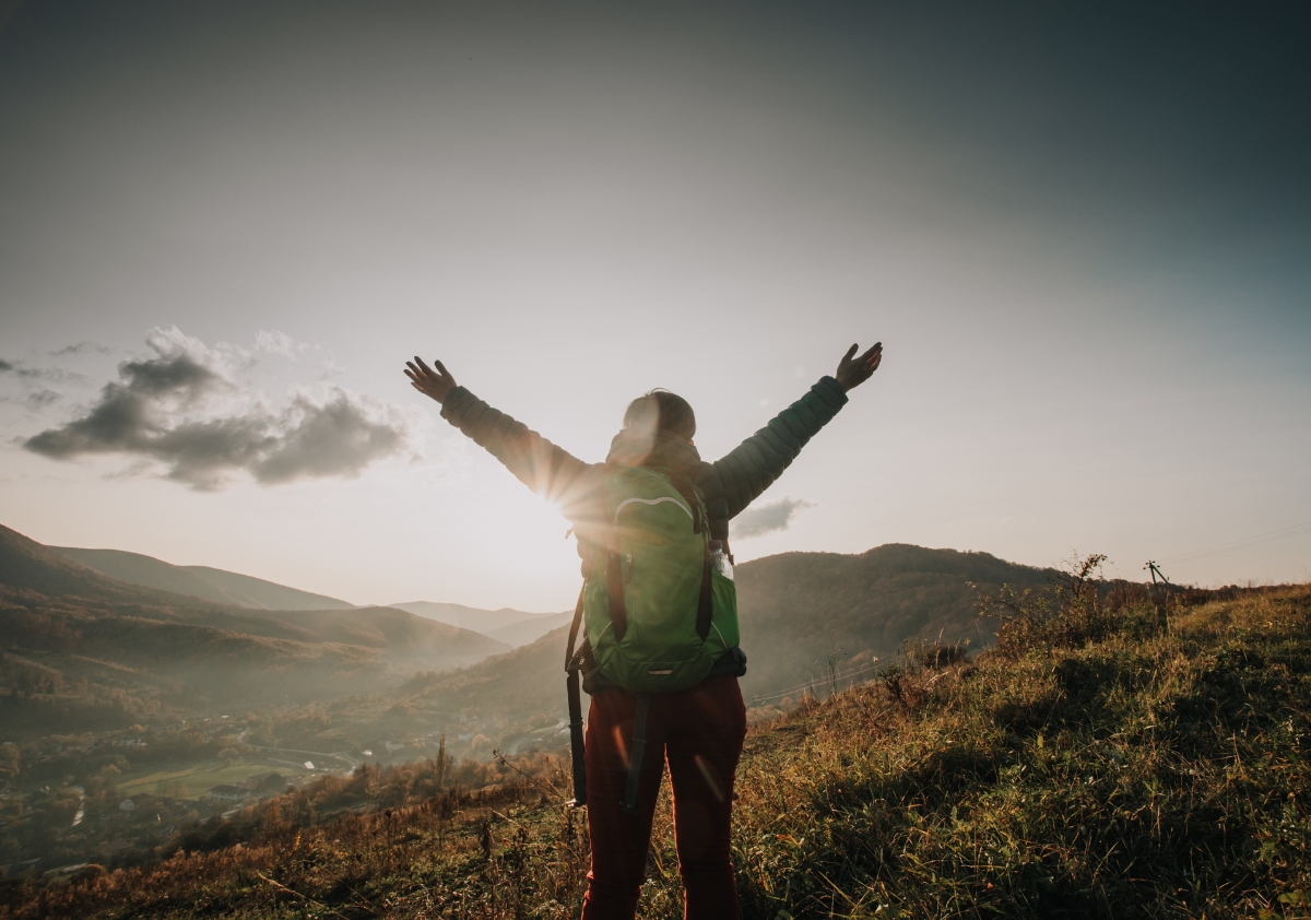 A person of color stands on top of a mountain with their arms outstretched taking in fresh air