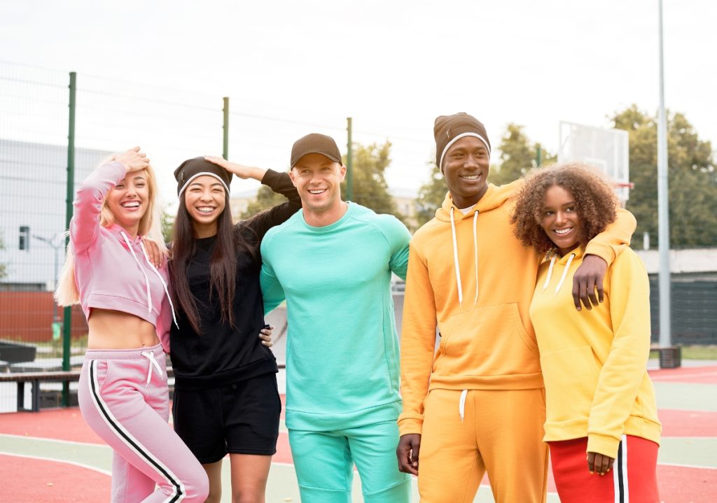 A group of fit multicultural millennials in workout attire posing with one another on the playground together