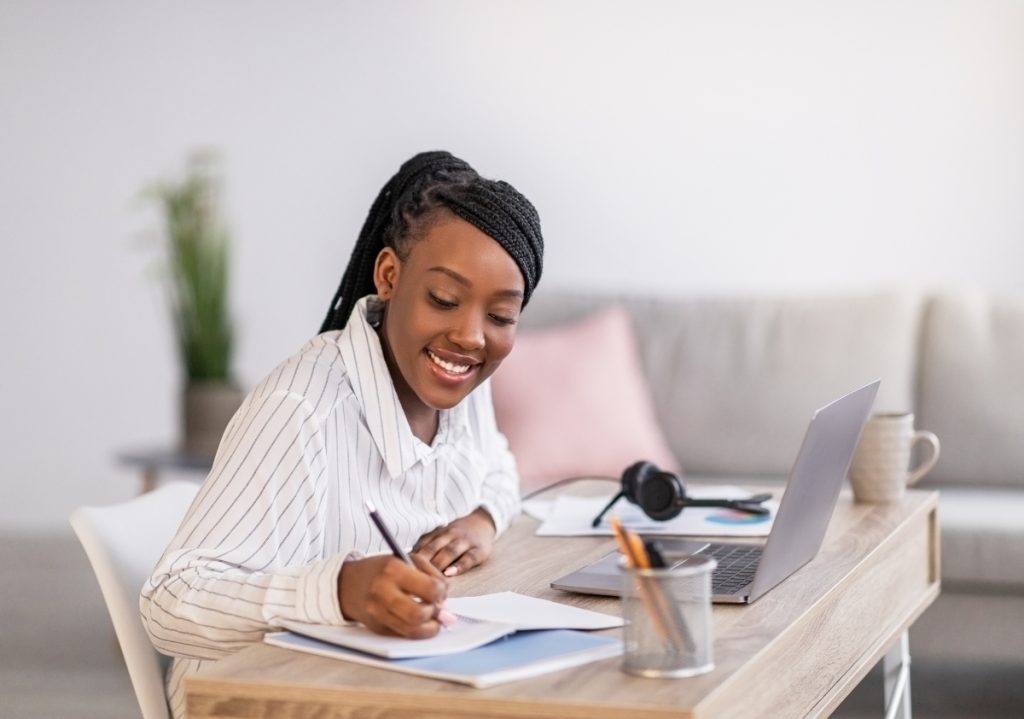 A professional woman of color with braids wearing a pinstripe button-up blouse sitting at her desk working on a brand storytelling idea.