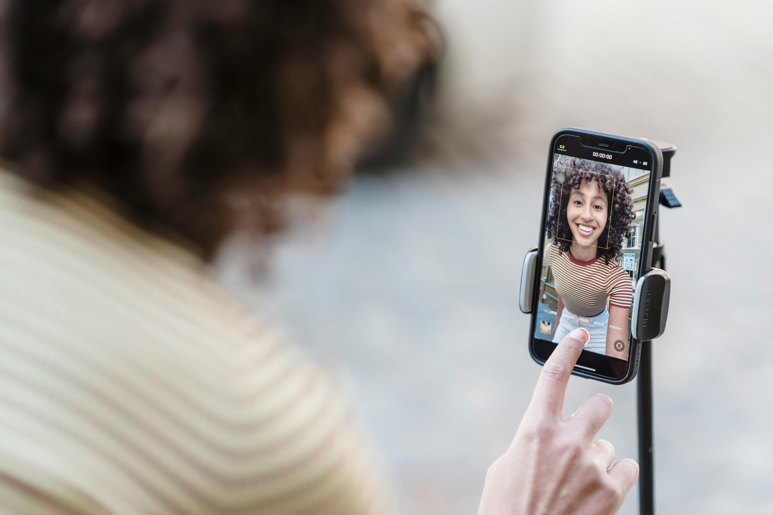 A woman operates a smartphone that's balanced on a tripod, filming herself.