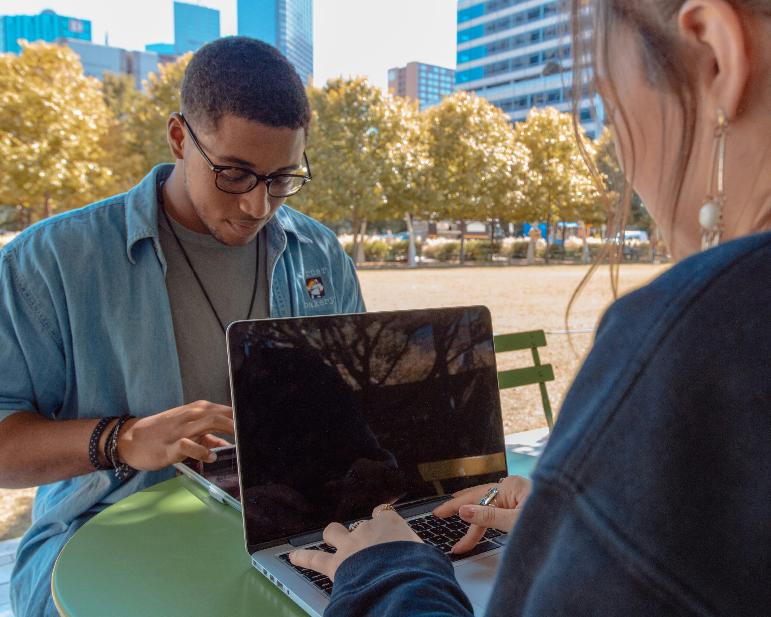 Two Gen Z individuals use laptops in a public park.